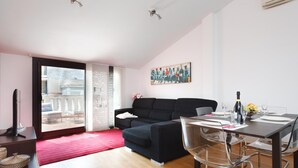 Una sala de estar moderna con un sofá negro, una mesa de comedor con sillas y un amplio ventanal con vistas a un balcón.