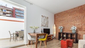 Een moderne woonkamer met een houten eettafel, stoelen, een televisie en een bakstenen muur.