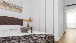 Een moderne slaapkamer met een groot bed, een nachtkastje met een bloevas en uitzicht op een gang.