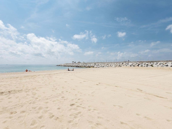 Una playa arenosa con huellas, un rompeolas rocoso y el océano al fondo.