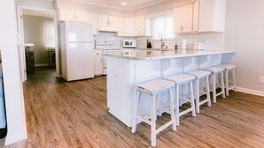 A modern kitchen with white cabinetry, a central island with bar stools, and a wooden floor. - Paradise Sands 5bed/3 bath+home office Sleeps 13  (Murrells Inlet)