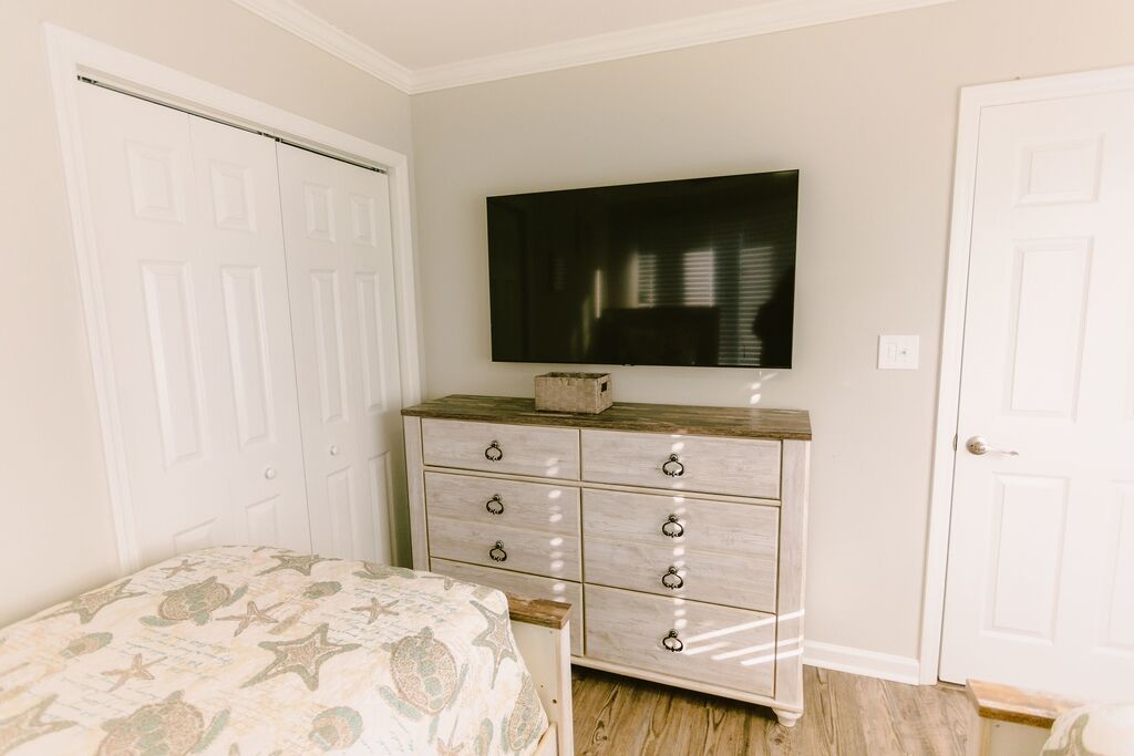 Une chambre à coucher avec un lit, une commode, un téléviseur et une porte.