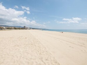 A wide, sandy beach with footprints, a clear sky, and distant buildings.