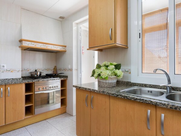 A kitchen with wooden cabinets, a stainless steel sink, a stove, and a window with blinds.
