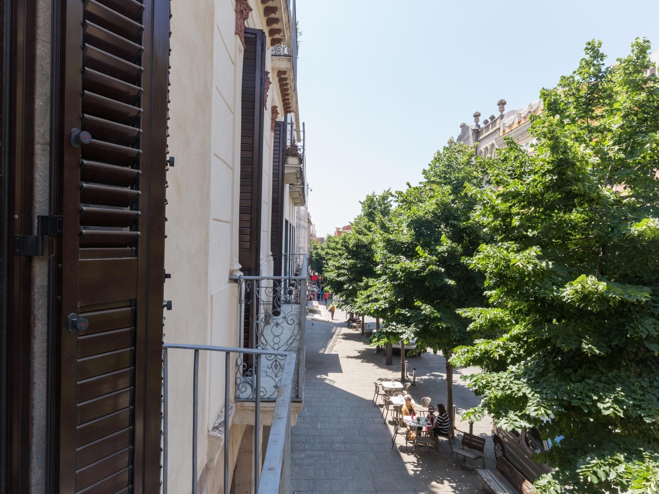 Een smalle straat met gebouwen aan beide kanten, een trottoir met bomen en terrasjes.