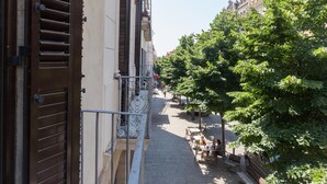 Una calle estrecha flanqueada por edificios, con aceras arboladas y terrazas de café al aire libre.