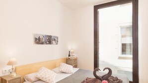 Un dormitorio con cama, mesita de noche, lámpara, un cuadro en la pared y ventana.