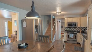 Una cocina moderna con una mesa de comedor de madera, una lámpara colgante negra y un refrigerador de acero inoxidable.