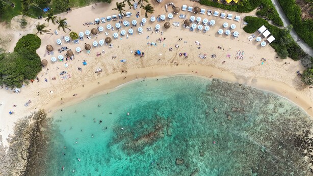 Vista aérea de uma praia com espreguiçadeiras, guarda-sóis e um mar azul-turquesa límpido.