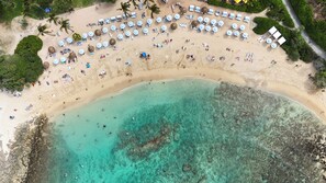 An aerial view of a beach with sun loungers, umbrellas, and a clear turquoise sea. - Hale Koa Newly updated condo with split AC (Kahuku)