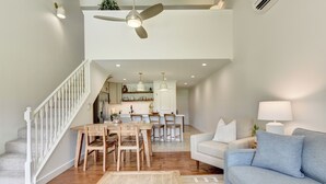 Uma sala de estar ampla com escada, mesa de jantar com cadeiras, sofá e ventilador de teto.