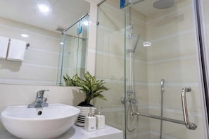 A modern bathroom with a glass-enclosed shower, a white sink, and a potted plant.