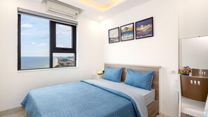 A bedroom with a large bed, a window with a city view, and three framed artworks on the wall. - Muong Thanh Apartment (Da Nang)