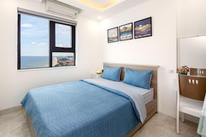 A bedroom with a large bed, a window with a city view, and three framed artworks on the wall.