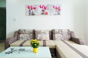 Un salon comprenant un canapé, une table basse ornée d’un vase avec une fleur jaune, et trois tableaux floraux encadrés accrochés au mur.