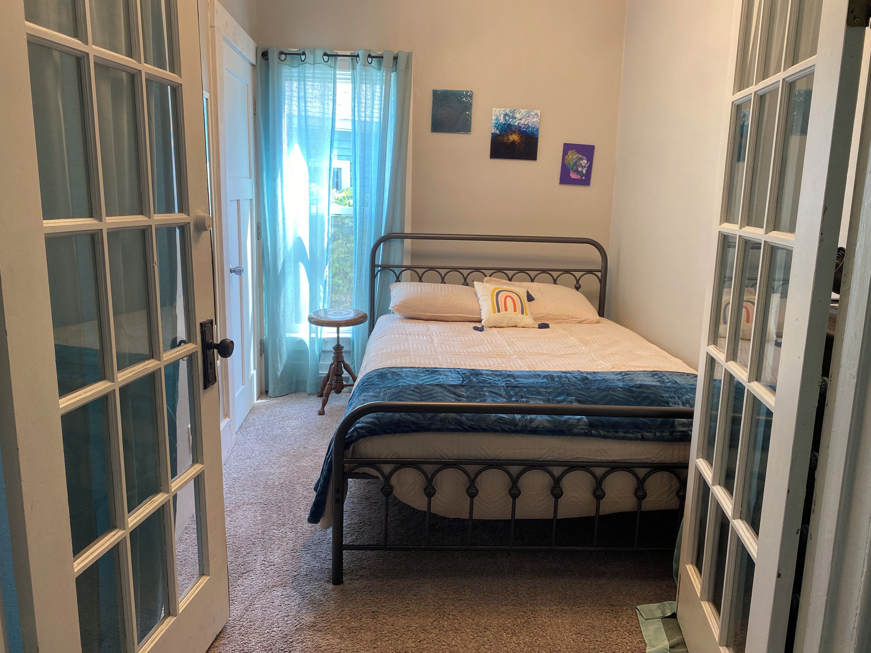 A bedroom with a bed, a window, a door, and a small table.
