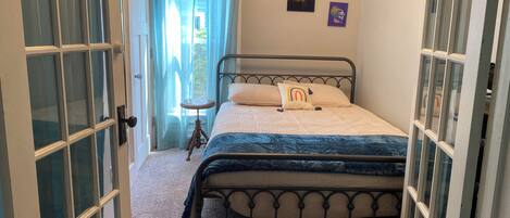 A bedroom with a bed, a window, a door, and a small table.