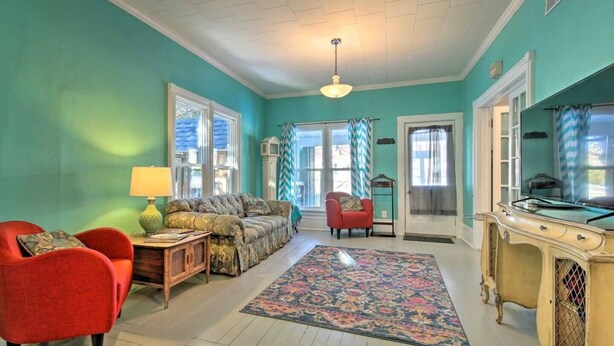 Una sala de estar con paredes verde mar, un tapete estampado, un sillón rojo, un sofá y una mesa de estilo antiguo.