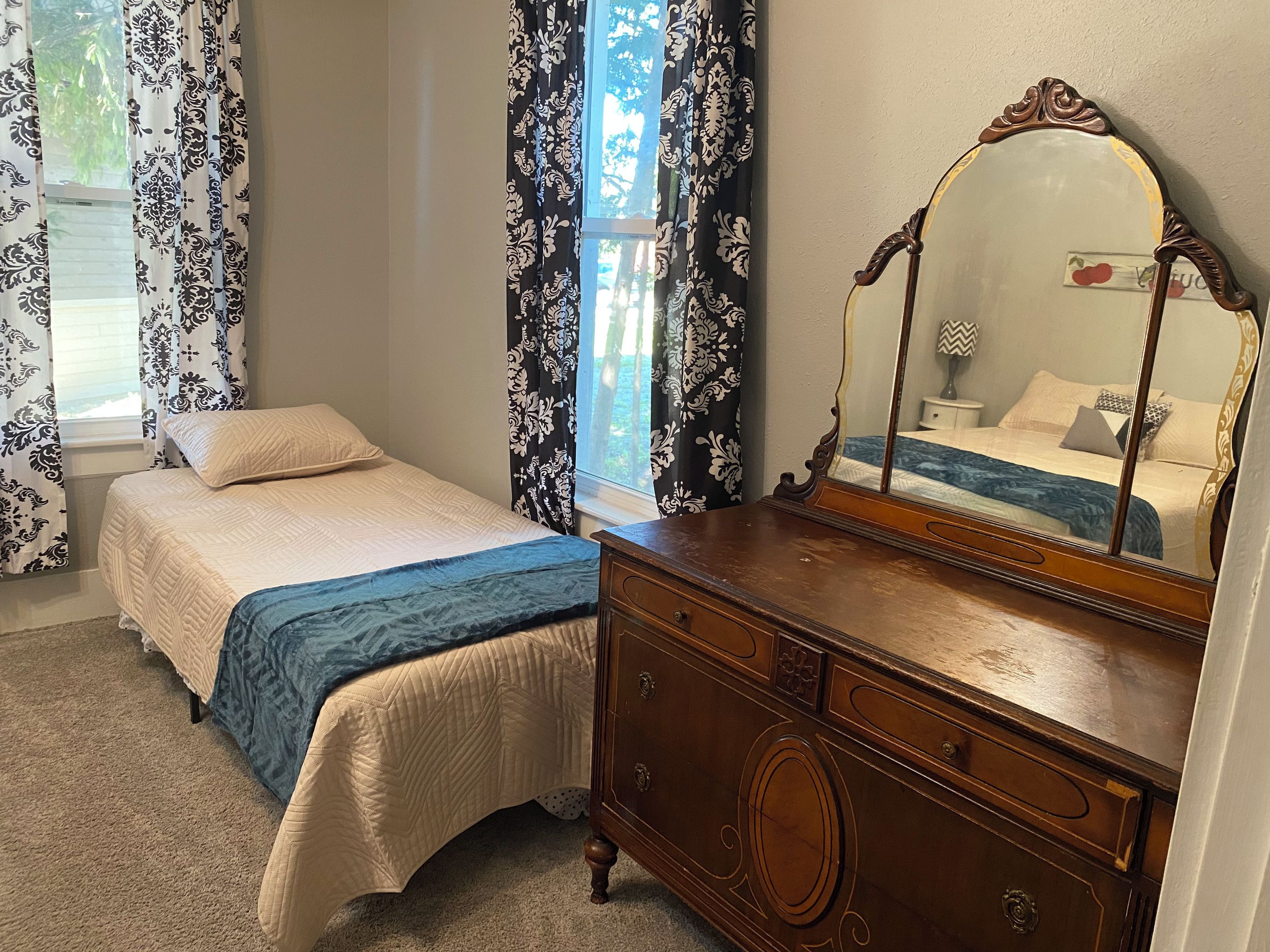 Une chambre à coucher avec un lit, une commode, un miroir et des rideaux.