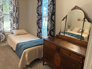 Een slaapkamer met een bed, een dressoir, een spiegel en gordijnen.