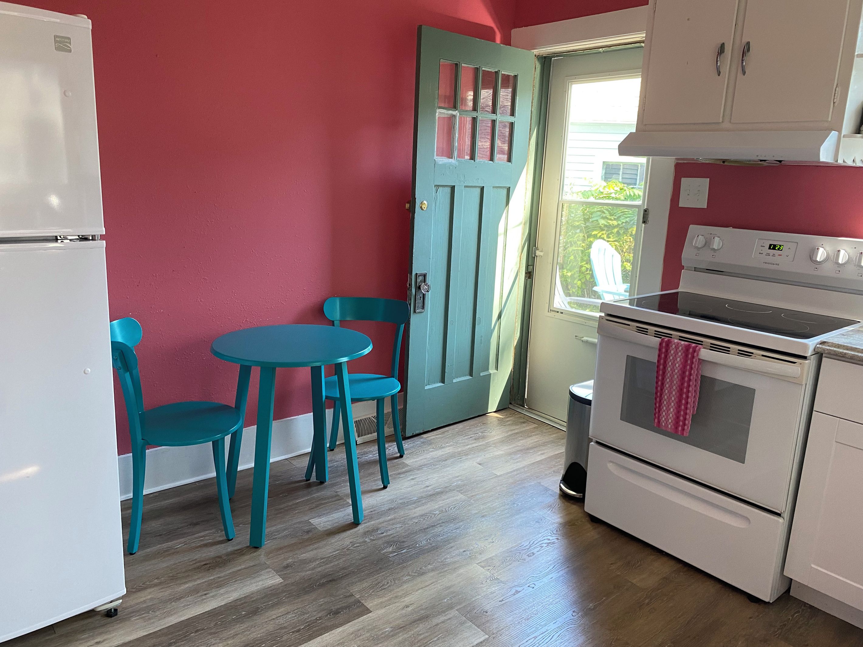 A compact kitchen with a refrigerator, stove, and teal chairs around a small table.
