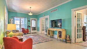 Un salón con paredes verde azulado, un sillón rojo, un televisor y una alfombra estampada.