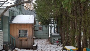 A wooden playhouse with a window, a bench, and a small table with chairs in a snowy backyard.