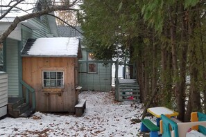 A wooden playhouse with a window, a bench, and a small table with chairs in a snowy backyard.