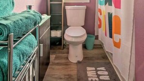 A bathroom with a pink wall, a white toilet, a sink with a mirror, and a shower curtain with colorful text.