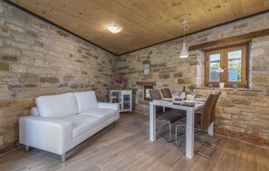 Quarto com parede de pedra, sofá branco, mesa de jantar com cadeiras e janela com vista.