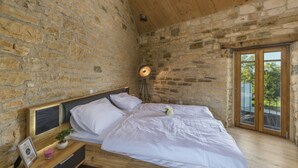 A bedroom with stone walls, a wooden ceiling, a bed with white linens, a bedside table with a lamp, and a view through a glass door. - Aquileia Residence # 2- peaceful, private garden, large pool, close to Grožnjan (Grožnjan)