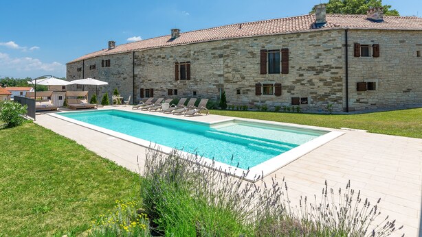 Un edificio de piedra con piscina, mobiliario exterior y césped bien cuidado.
