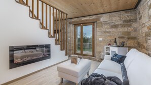 Un salón moderno con una escalera de madera, paredes de piedra, un sofá blanco y un televisor de pantalla plana montado en la pared.