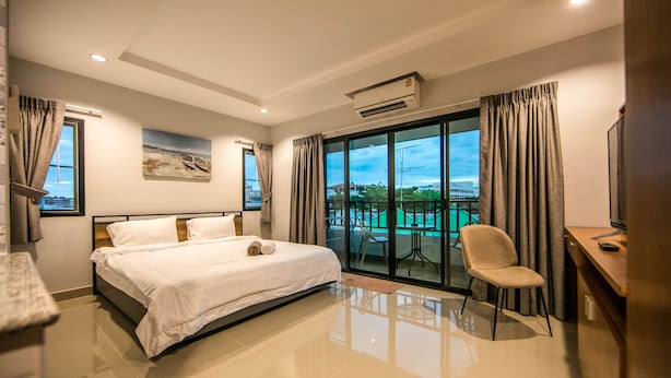 Una habitación de hotel moderna con una cama grande, un escritorio y una silla. Cuenta con un balcón con mesa y sillas fuera de la ventana.