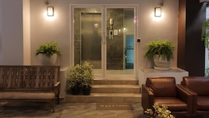Una entrada moderna con puerta de vidrio, un banco, dos plantas en macetas y un felpudo.