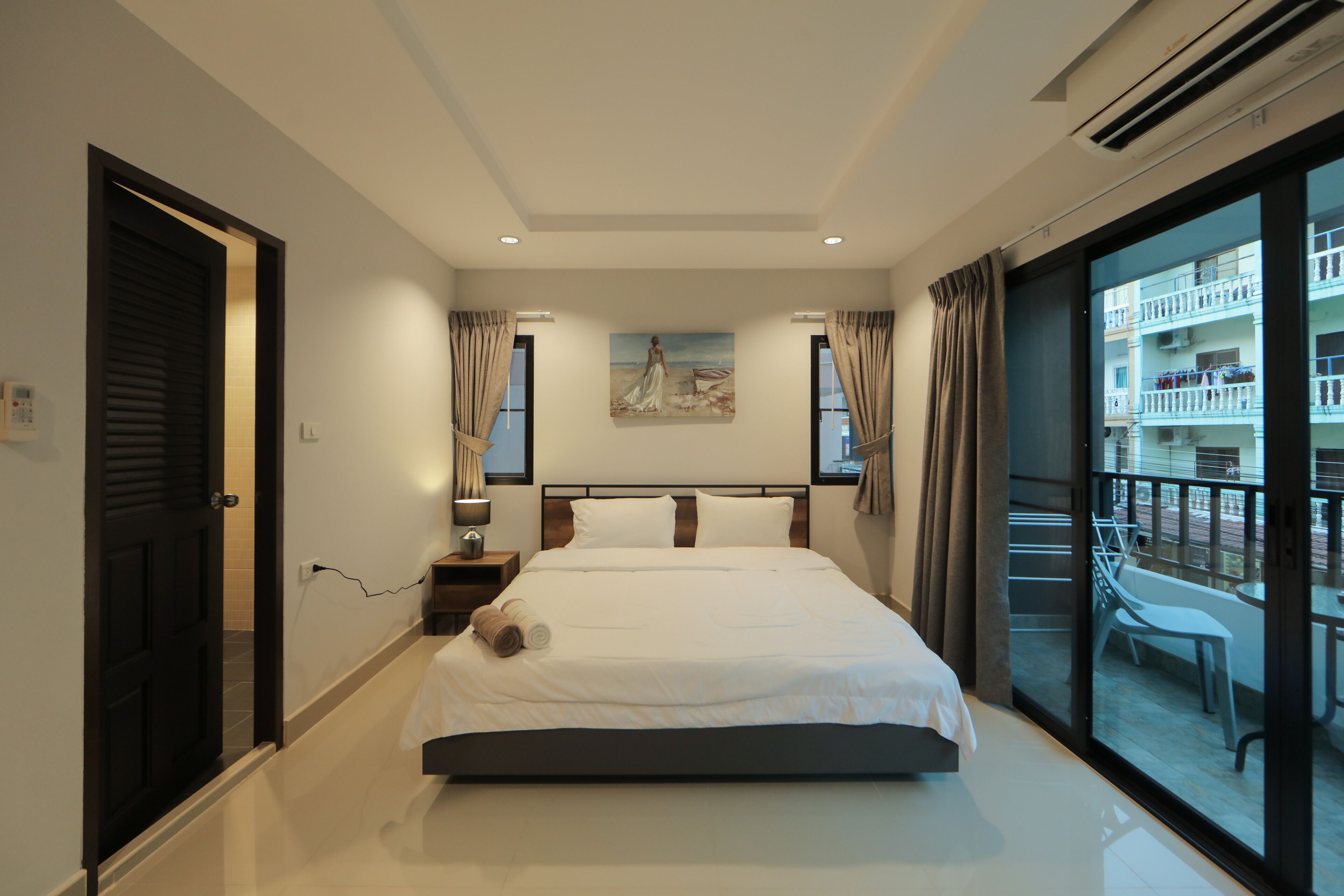 A modern hotel room with a large bed, a painting on the wall, and a balcony with outdoor furniture.
