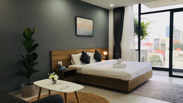 Una habitación de hotel moderna con una cama grande, una mesita de noche, una pequeña mesa redonda y una planta en maceta.