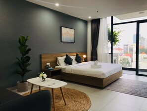 A modern hotel room with a large bed, a bedside table, a small round table, and a potted plant. - The Green House Binh Duong (Ho Chi Minh City)