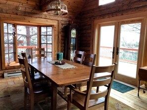 A wooden dining room with a large table and chairs, large windows, and a chandelier. - Cliffside Log Cabin w/  Large Deck for Enjoying Spectacular Views & Wildlife (Boise)