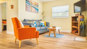 Una sala de estar con sofá, sillón, mesa de centro, televisor y estantería.
