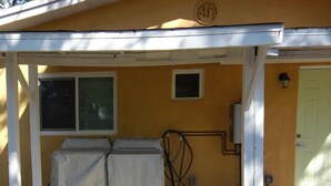 Un espacio al aire libre techado con dos elementos cubiertos, posiblemente equipo de lavandería, y una ventana pequeña.
