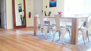 Un comedor con una mesa de madera y sillas blancas, un extintor y un cuadro en la pared.