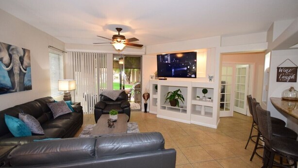 A living room with a black leather sofa, a coffee table, a TV, and a ceiling fan. - PRIVATE GATED VACATION CONDO  WITH HEATED POOL, SPA, FITNESS ROOM, PATIO, GARAGE (Mesa)