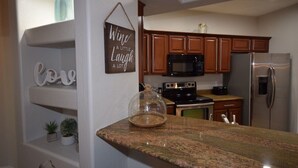 A kitchen with wooden cabinets, a stainless steel refrigerator, a microwave, and a coffee maker on the counter. - PRIVATE GATED VACATION CONDO  WITH HEATED POOL, SPA, FITNESS ROOM, PATIO, GARAGE (Mesa)