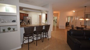 A modern kitchen with a central island, bar stools, and a dining area with a black leather couch. - PRIVATE GATED VACATION CONDO  WITH HEATED POOL, SPA, FITNESS ROOM, PATIO, GARAGE (Mesa)