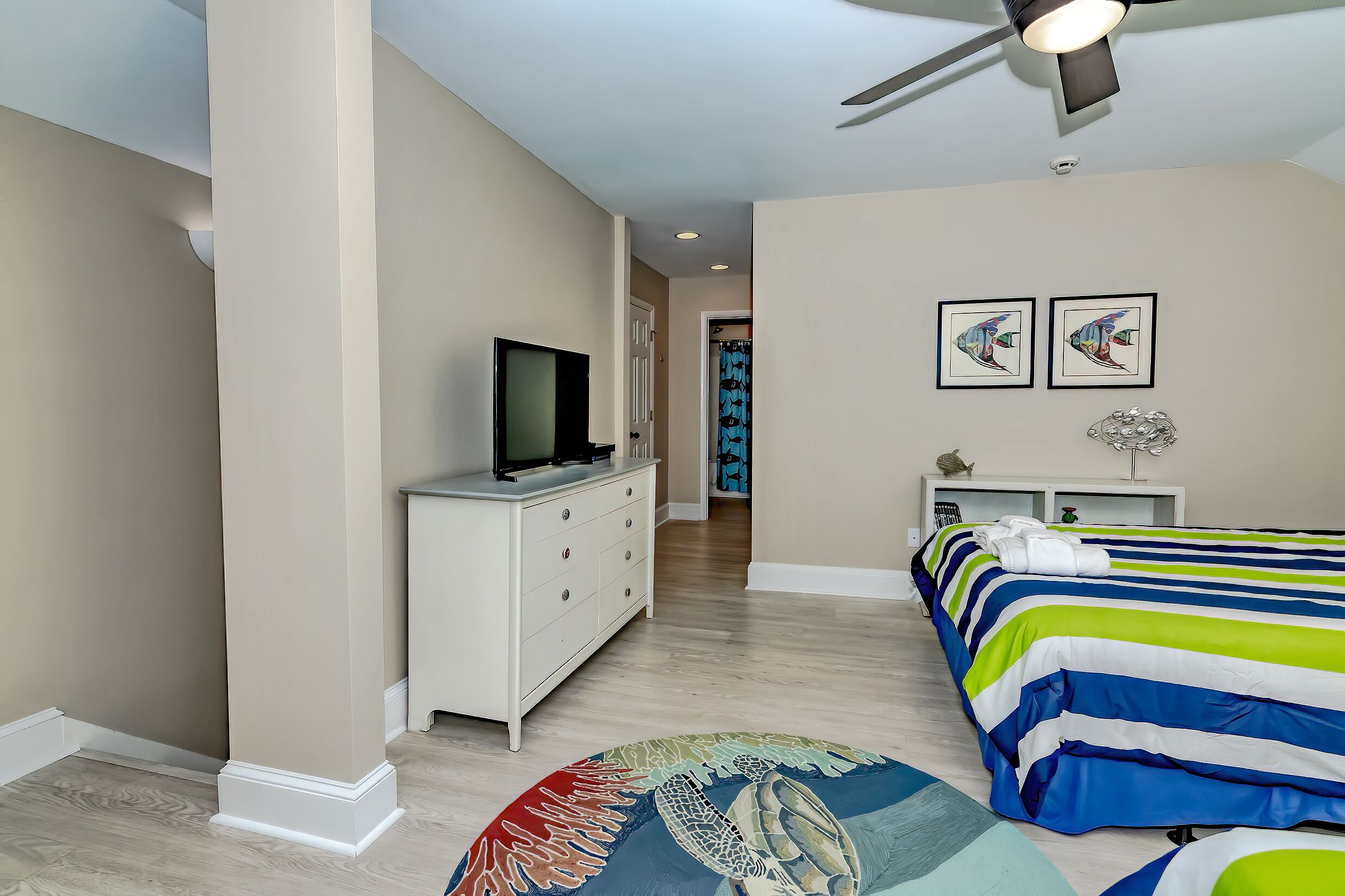 A bedroom with a bed, a TV on a dresser, and a ceiling fan.