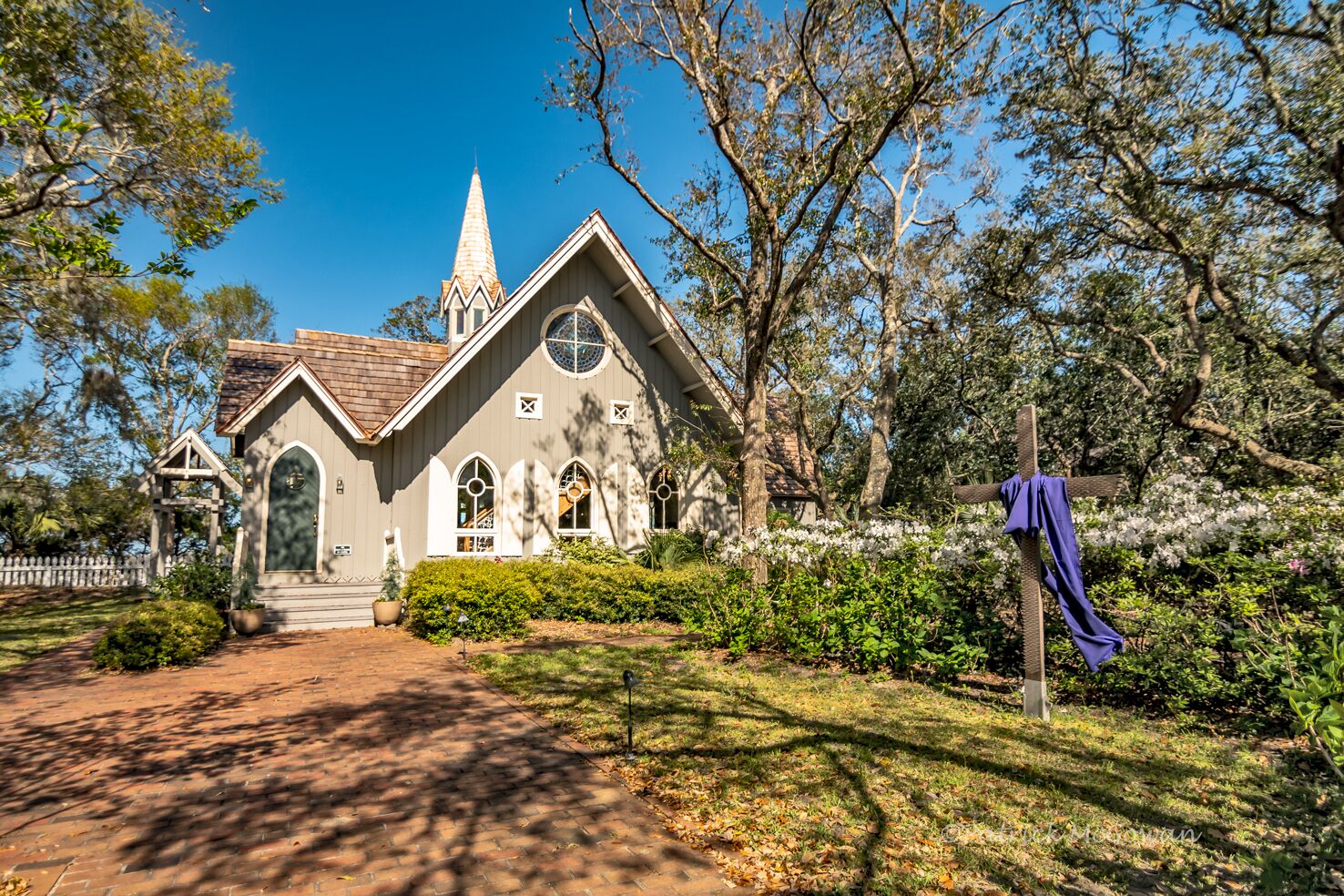 A church with a pointed steeple, arched windows, and a brick pathway leading to the entrance.