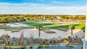 A golf course with sand bunkers, palm trees, and houses in the background.
