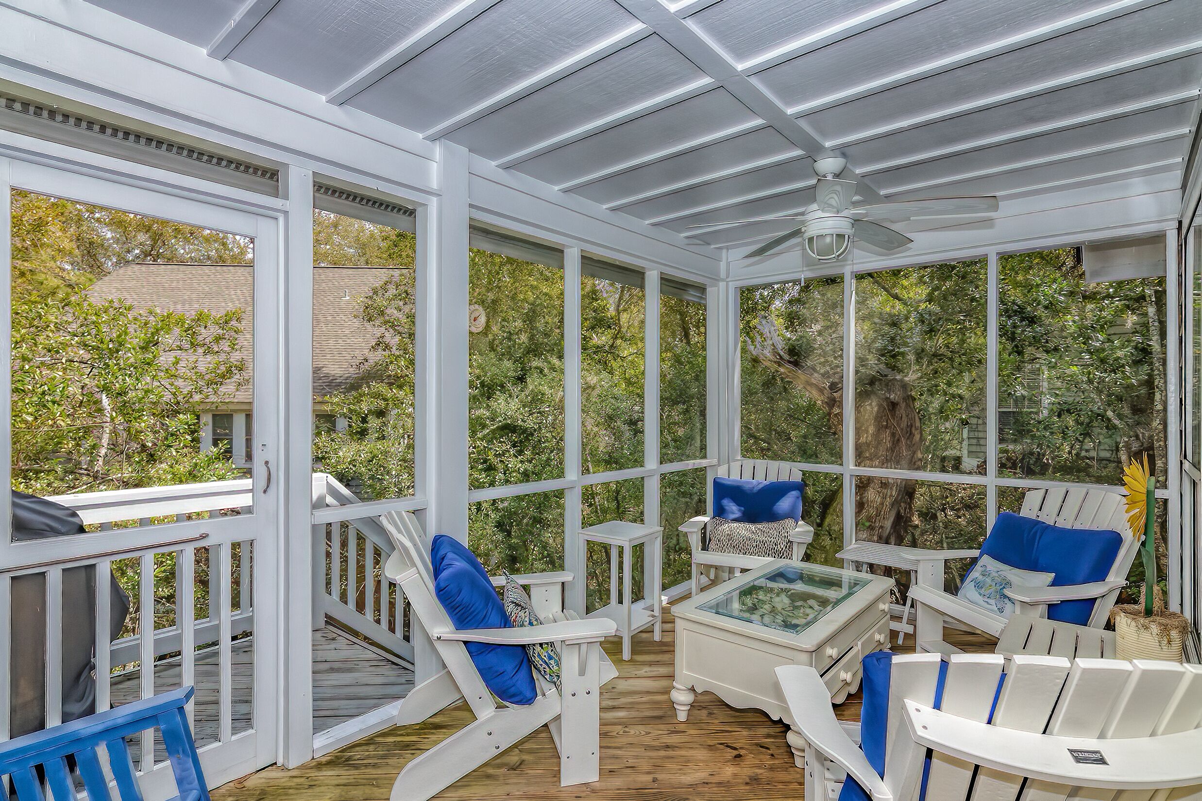 A covered outdoor area with white furniture and a glass table, surrounded by white railings and large windows.
