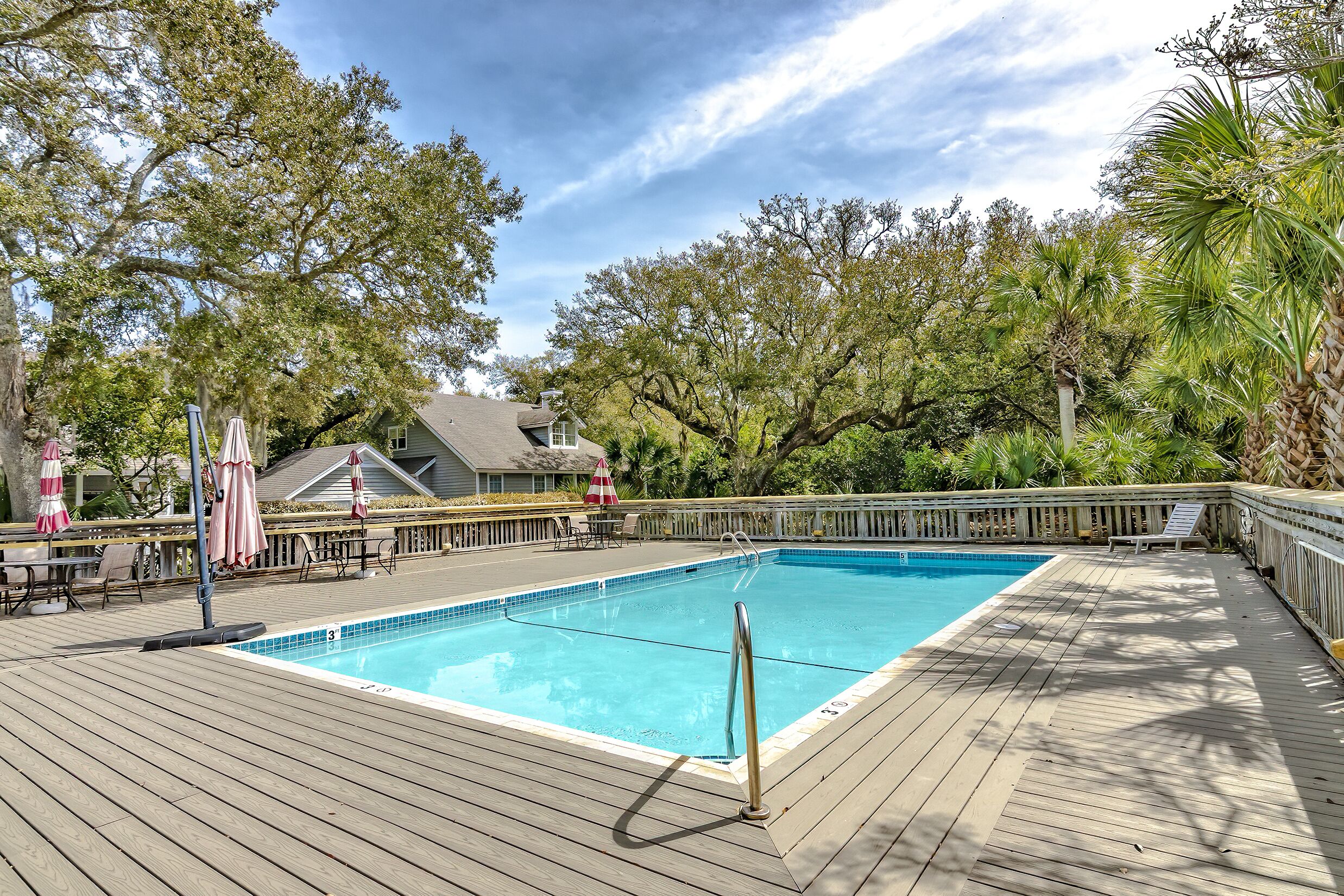 A wooden deck with a swimming pool, surrounded by trees and outdoor furniture.